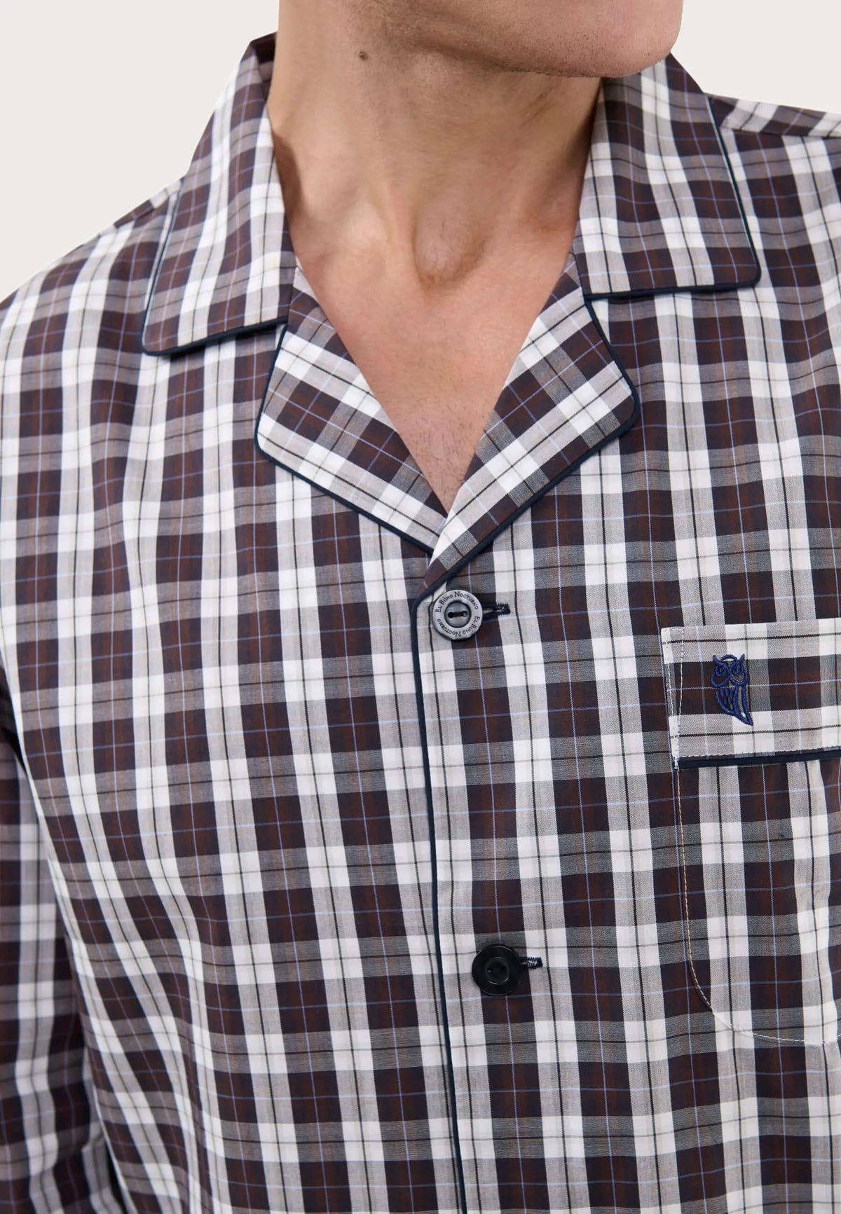 Pijama de hombre con cuello solapa, estampado de cuadros en marrón, blanco y azul, botones oscuros y bolsillo bordado.