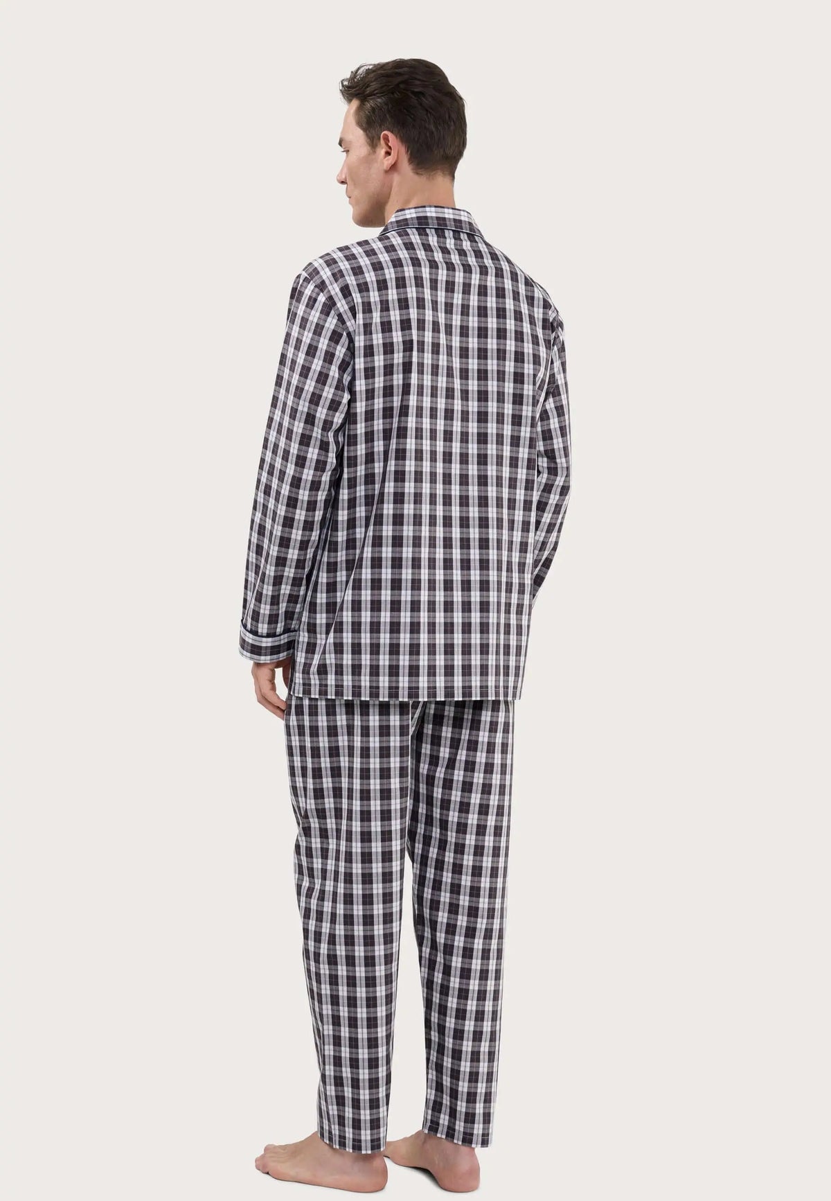 Hombre de espaldas con pijama largo de cuadros en tonos burdeos, gris y blanco, diseño de solapa y tejido de popelín.