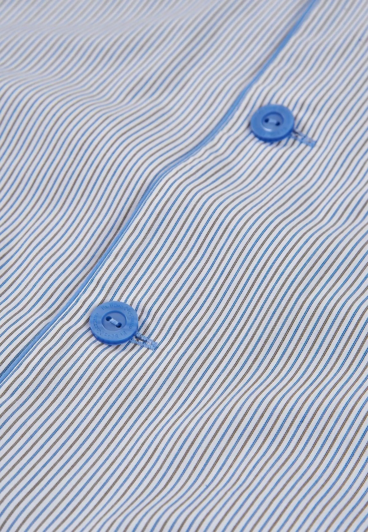 Detalle de pijama de algodón con rayas finas azules y beige, tejido liso y botones redondos azules con logo grabado.