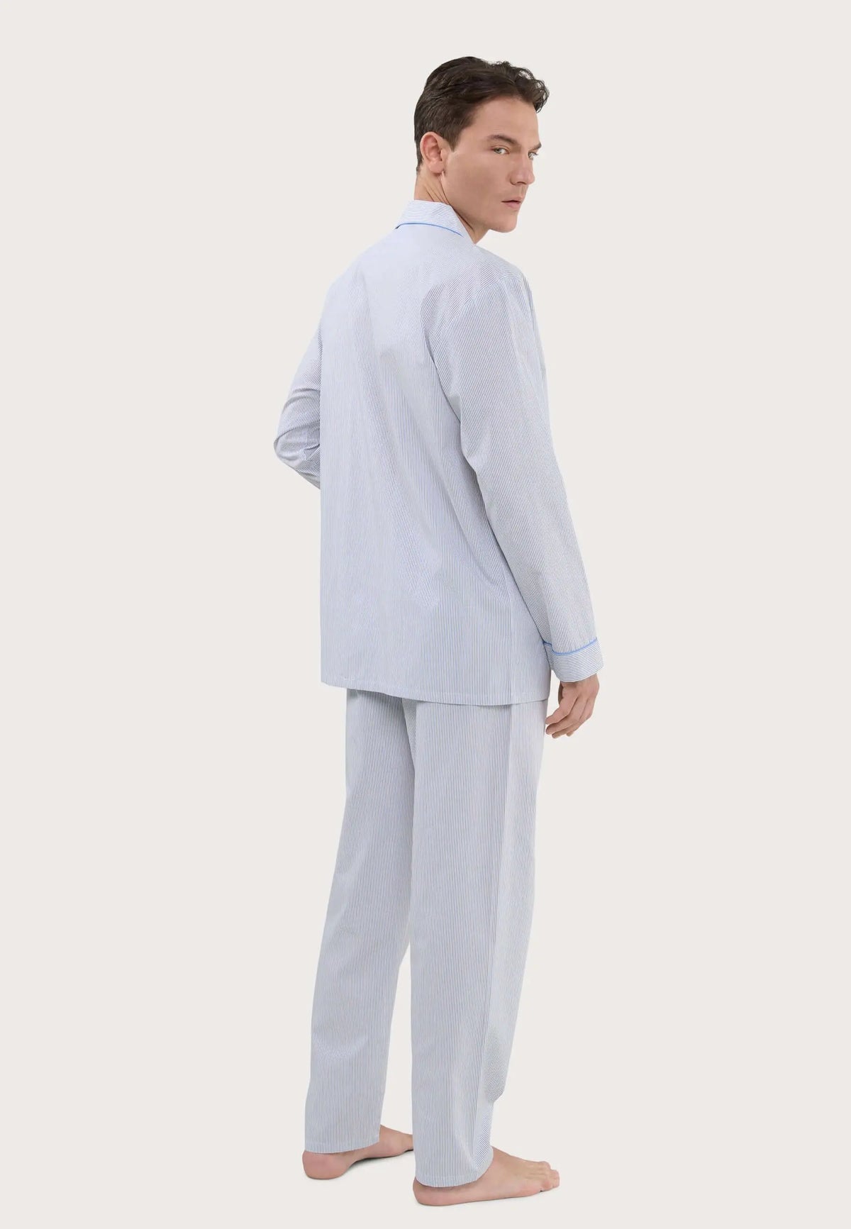 Hombre con pijama largo de rayas beige y azul, estilo clásico con solapa y ribetes azules, sobre fondo blanco.