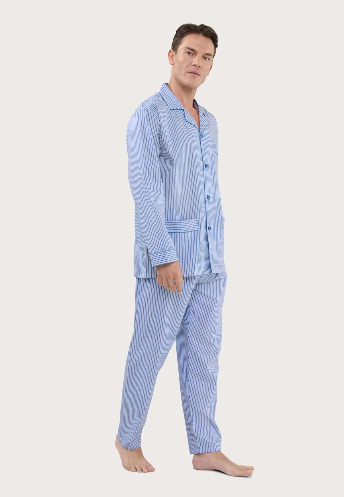 Hombre con pijama largo de botones, estampado de rayas verticales azul claro y blanco, cuello solapa y bolsillos.