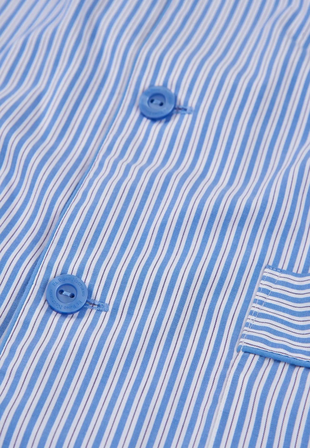 Detalle de pijama de algodón a rayas azules y blancas, con botones circulares azules y bolsillo lateral con solapa.