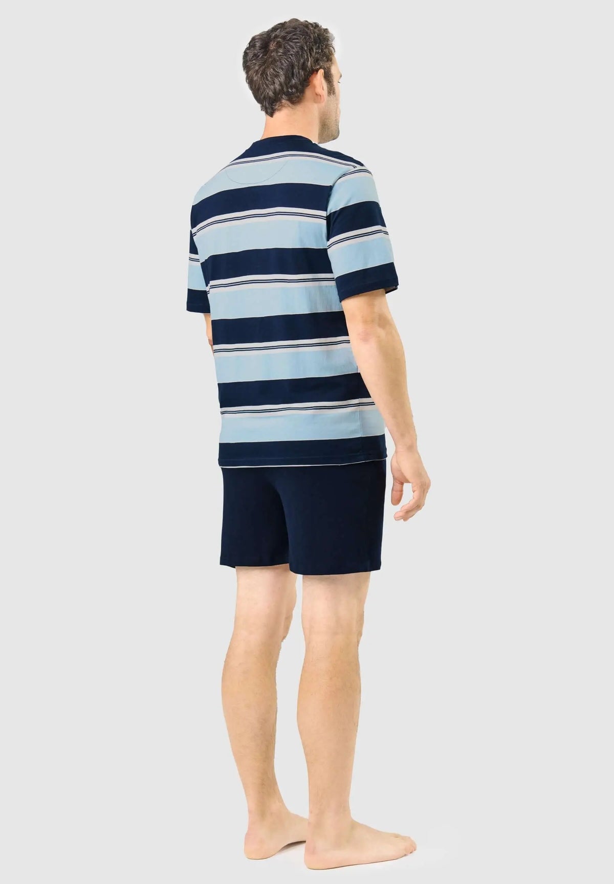 Hombre de espaldas con pijama corto de camiseta a rayas azules y pantalón corto liso azul marino El Búho Nocturno.