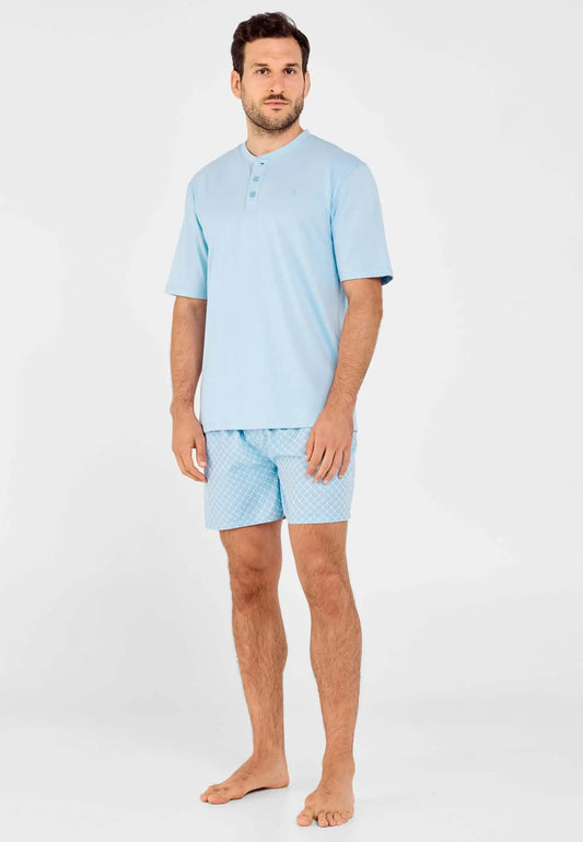Pijama corto hombre: camiseta azul de punto con botones y pantalón azul claro estampado. Modelo de pie.