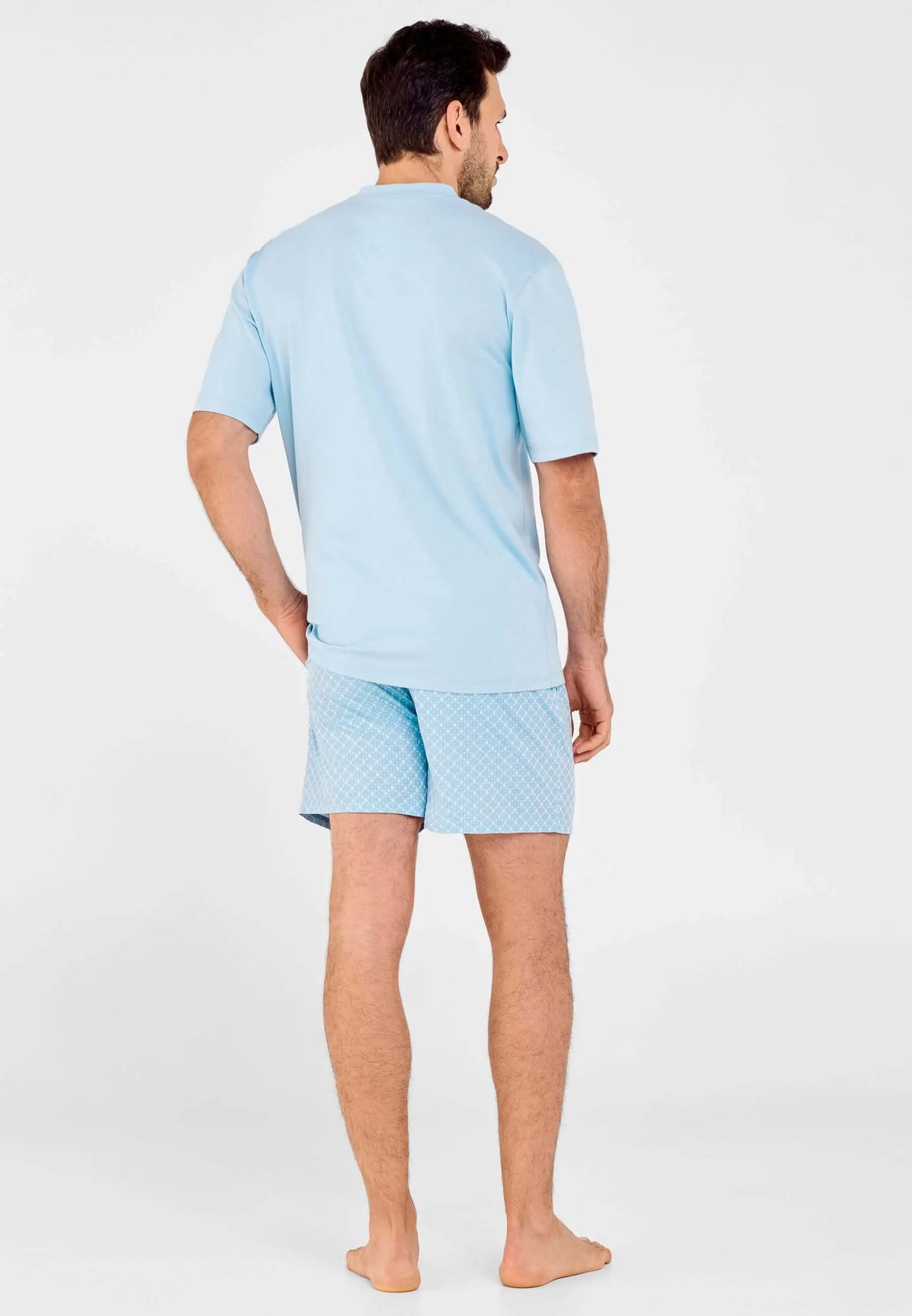 Pijama corto de hombre: camiseta azul lisa y pantalón con estampado geométrico, modelo de espaldas.