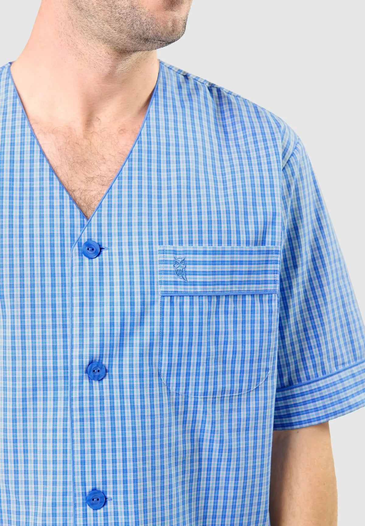 Pijama de hombre azul a cuadros, cuello pico, botones, manga corta y bolsillo con logo bordado de El Búho Nocturno.