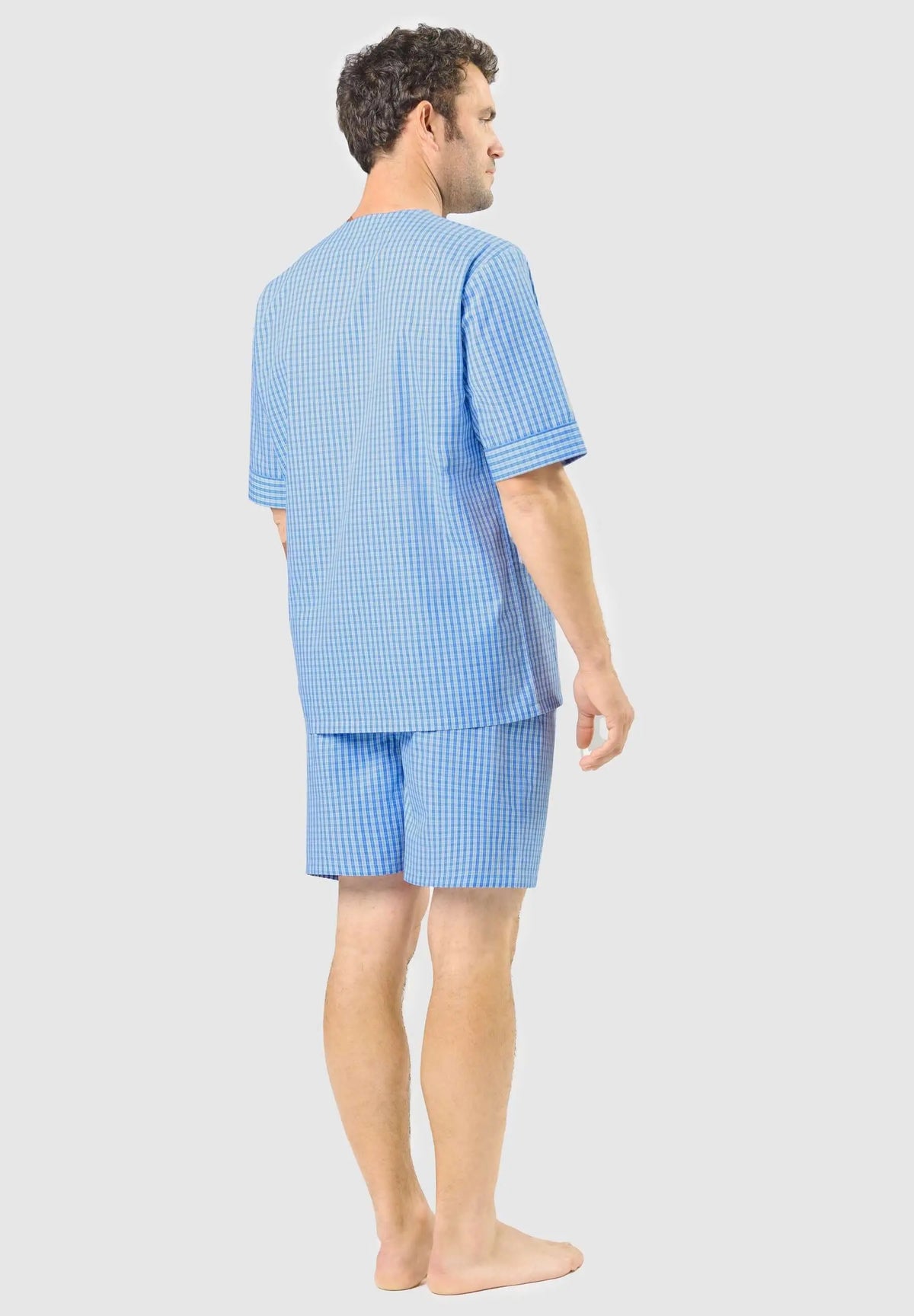 Hombre de espaldas con pijama corto de cuadros azules y blancos, camiseta de manga corta y pantalón corto de algodón.