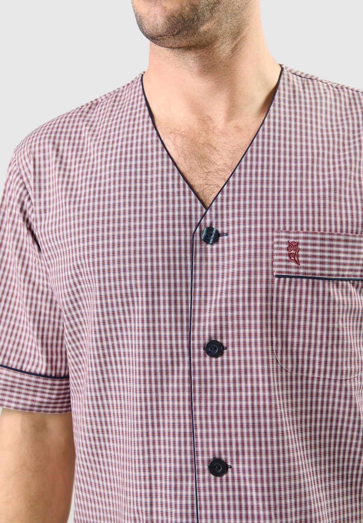 Pijama de hombre a cuadros rojos y blancos, cuello en V, manga corta, botones oscuros y bolsillo con logo bordado.