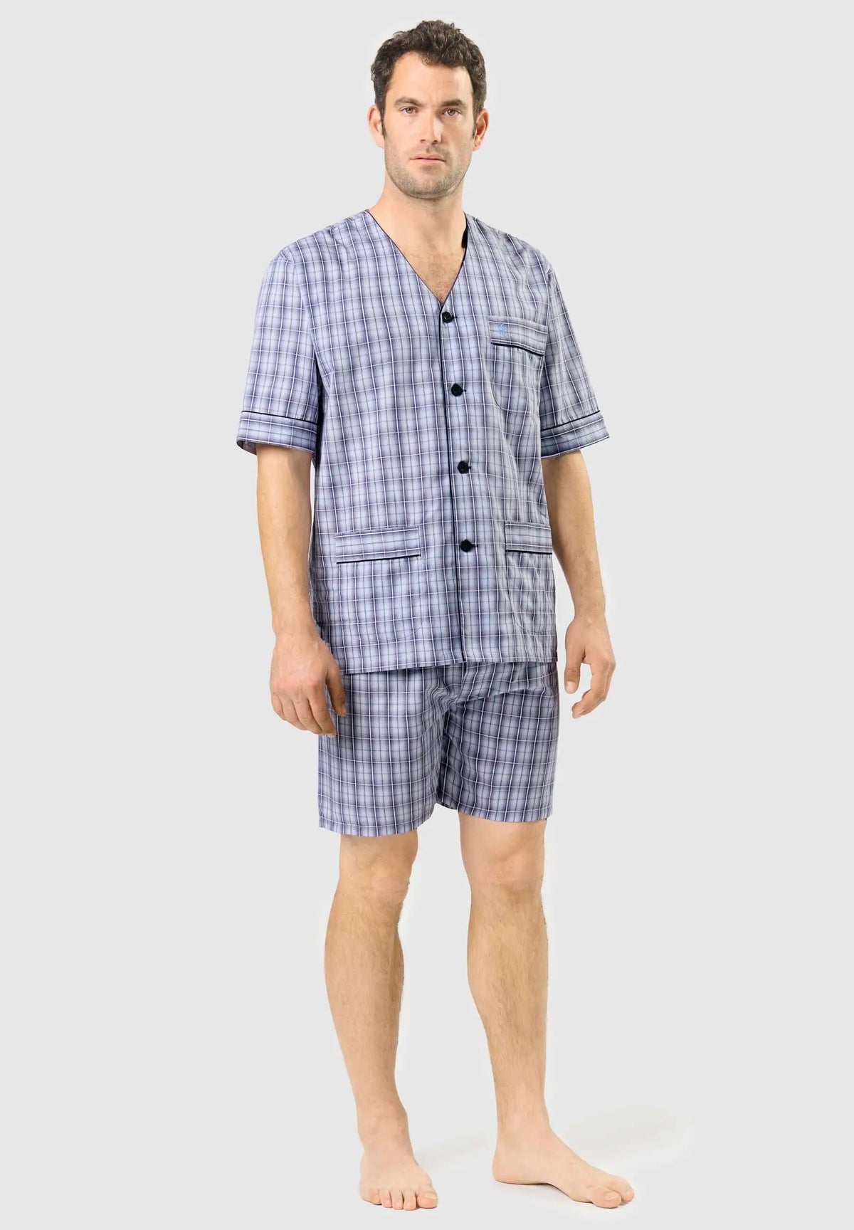 Pijama corto de hombre, cuello pico, botones, bolsillos y estampado de cuadros azul y gris sobre fondo claro.