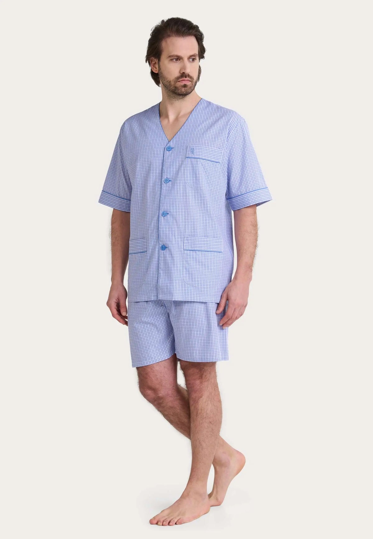Hombre con pijama corto de cuadros azules, cuello en pico, botones y bolsillos, tejido de popelín estilo judo.