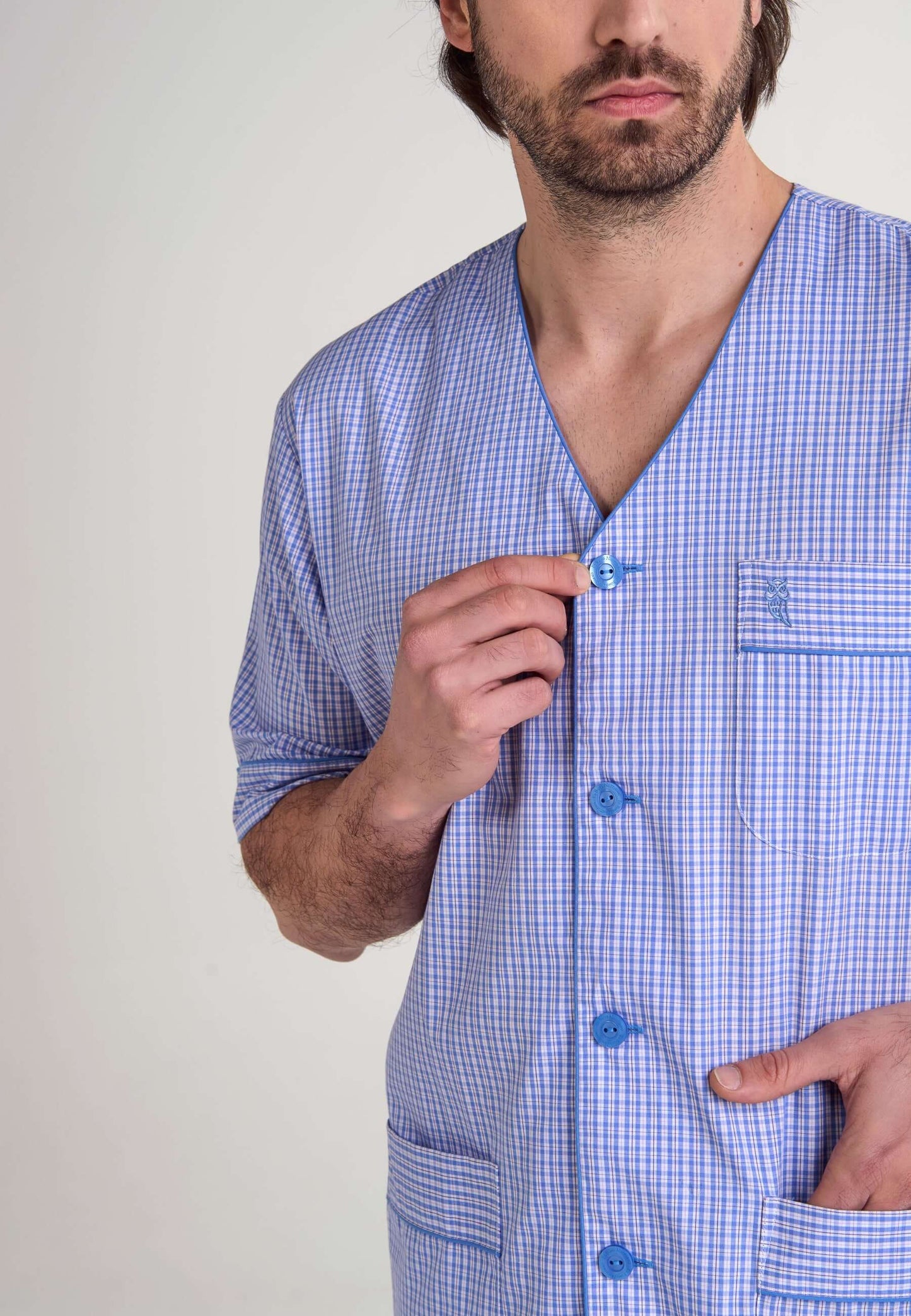 Pijama de hombre azul y blanco a cuadros con cuello en V, botones, bolsillo con logo de búho bordado y manga corta.