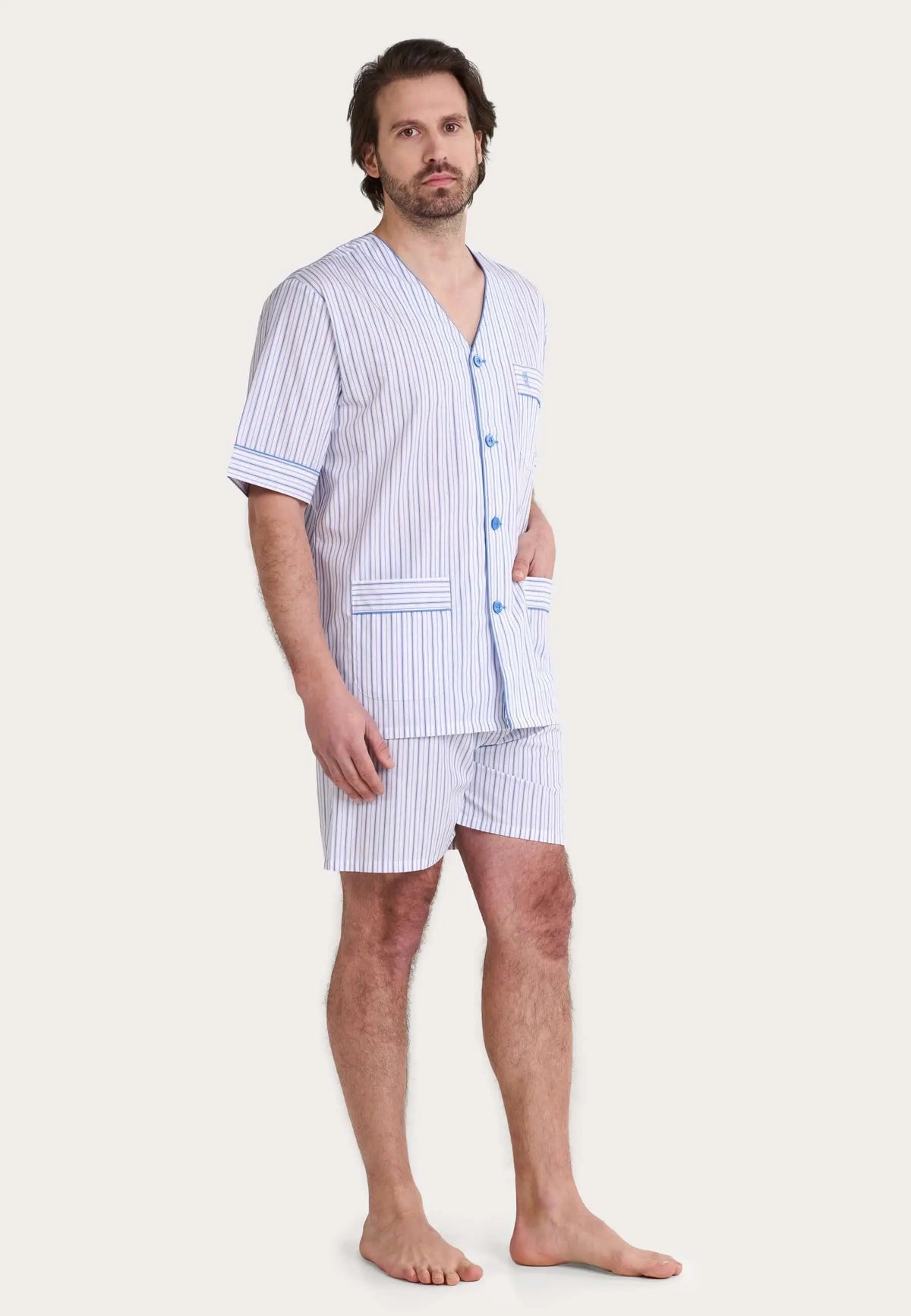 Modelo con pijama corto de hombre, cuello pico, botones, bolsillos y estampado de rayas verticales azul y blanco.