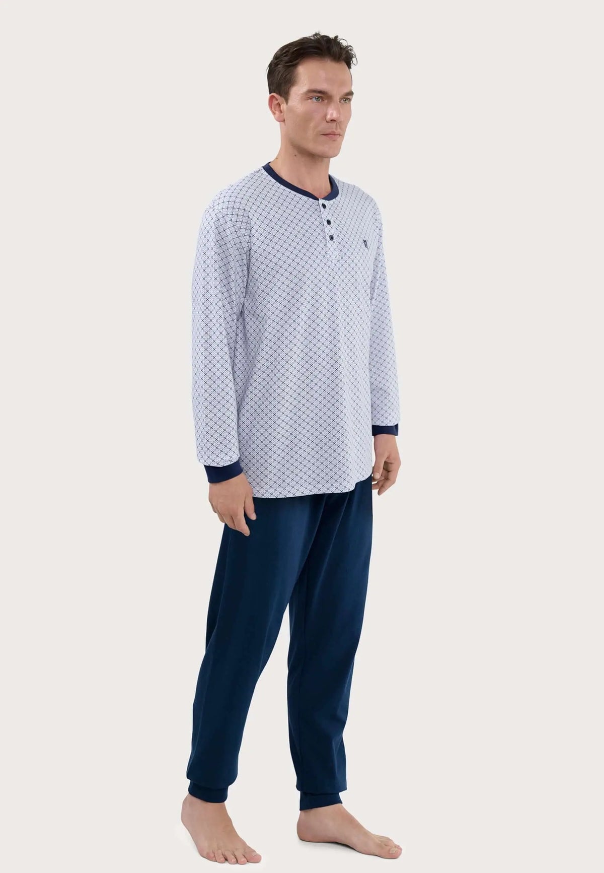 Hombre viste pijama largo de algodón: camiseta estampada de rombos con botones y pantalón azul marino liso de punto.