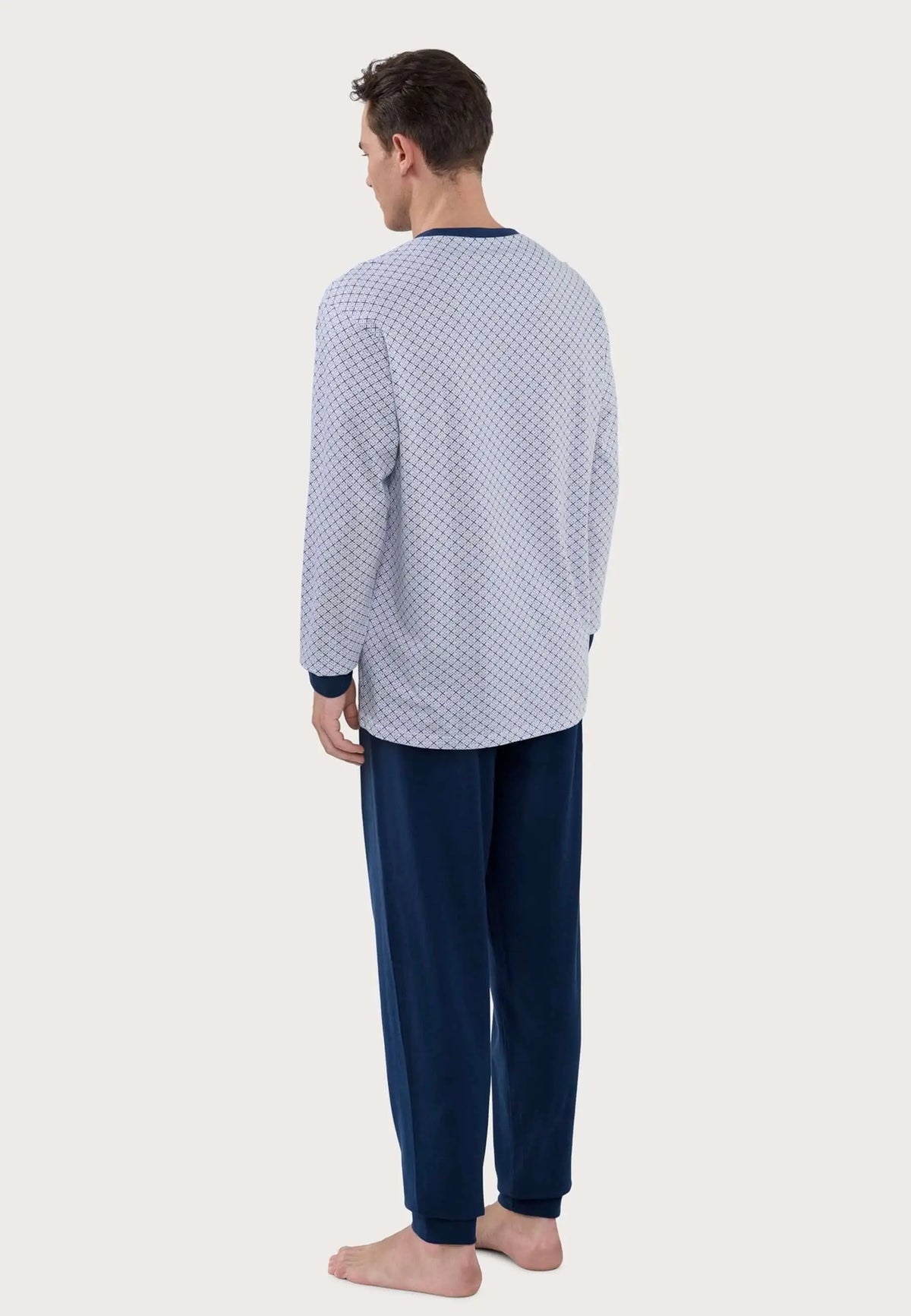 Hombre vistiendo pijama largo con camiseta estampada geométrica azul y blanca y pantalón azul marino liso.