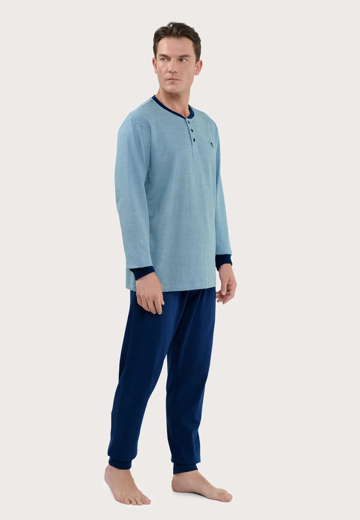 Hombre viste pijama largo azul: camiseta estampada con tapeta de botones y puños oscuros, pantalón liso a juego.
