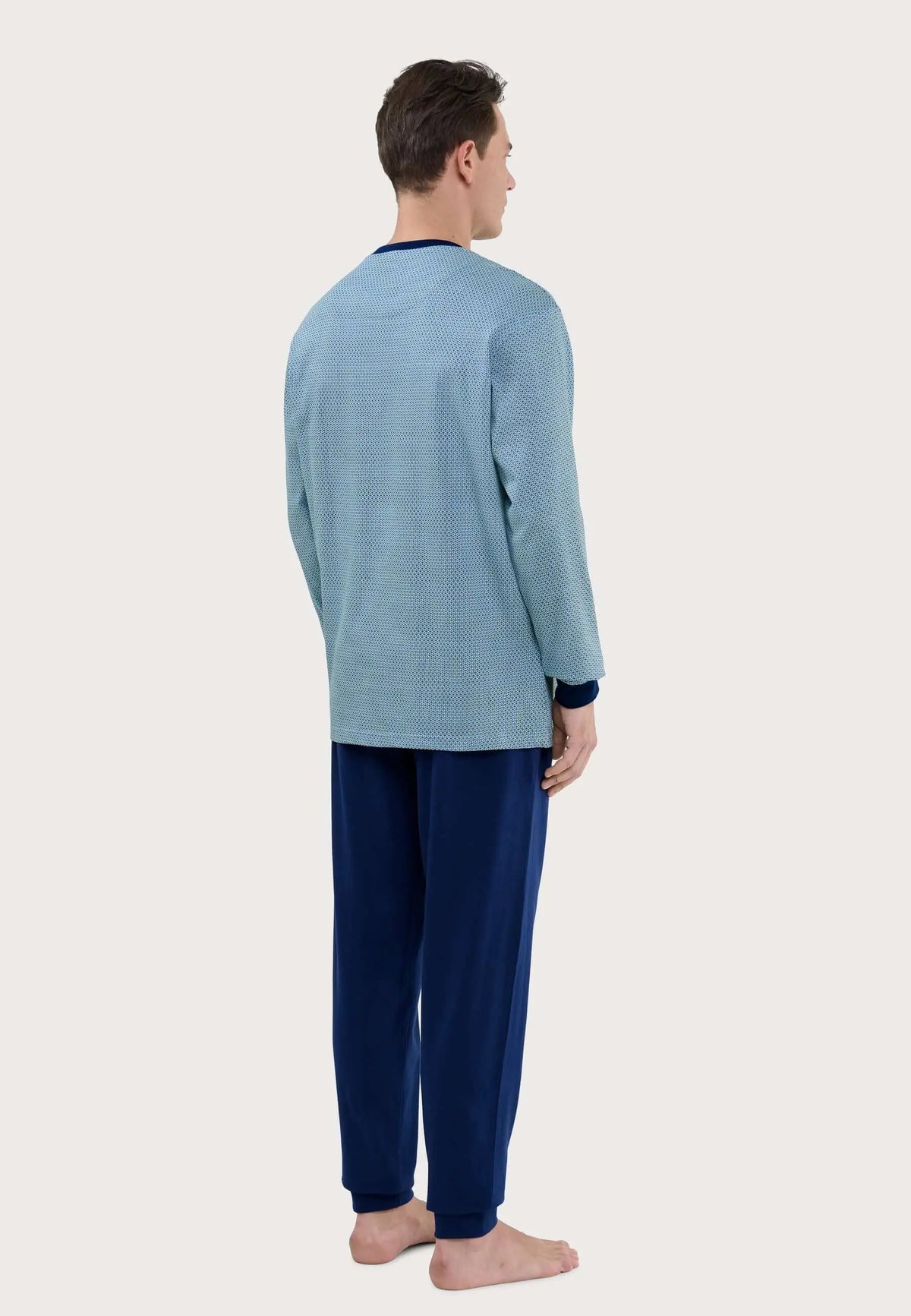 Hombre de espaldas vistiendo pijama largo: camiseta azul estampada de manga larga y pantalón liso azul marino con puños.