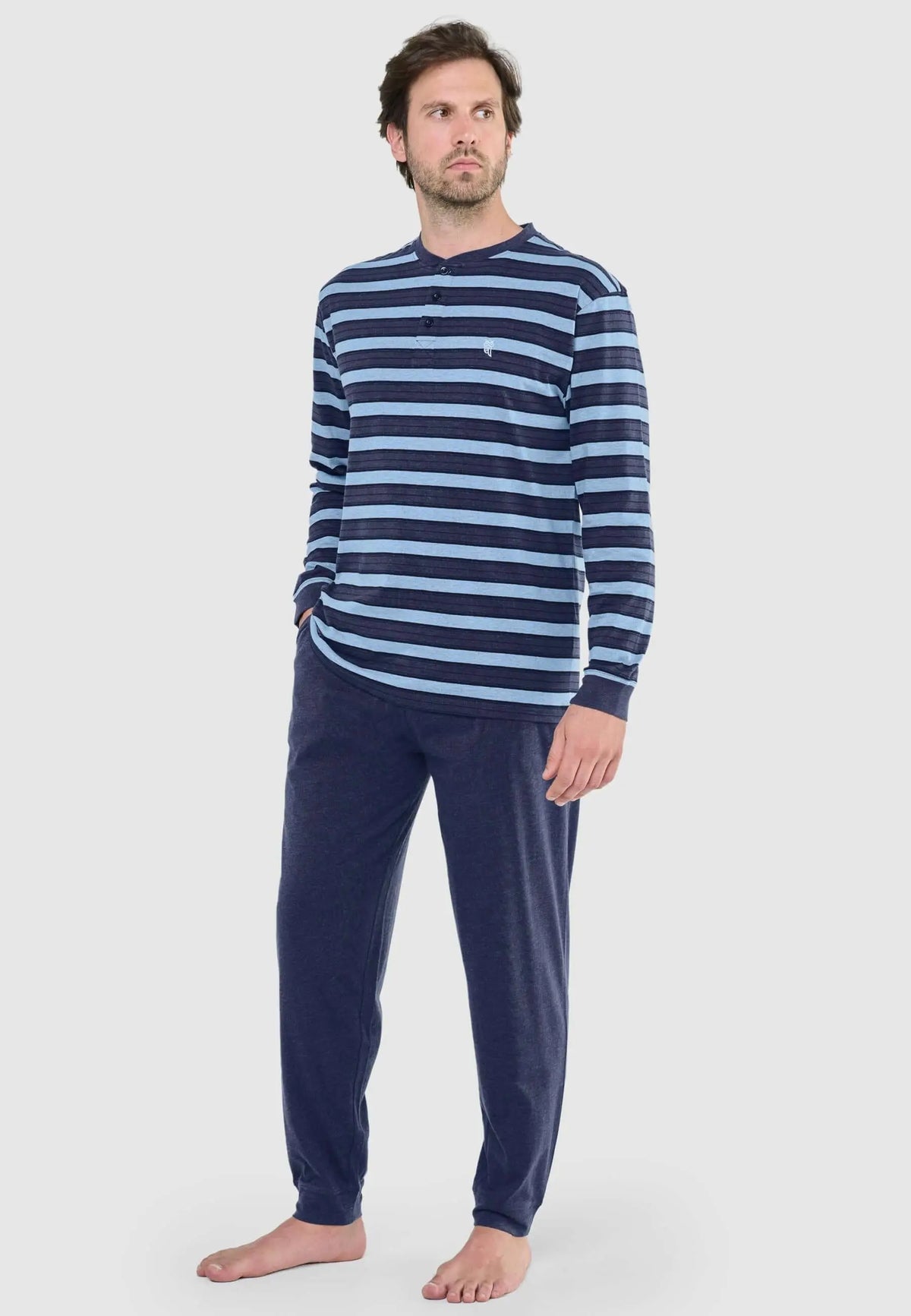 Hombre con pijama largo de rayas azul y marino, camiseta de manga larga con tapeta de botones y pantalón liso azul.