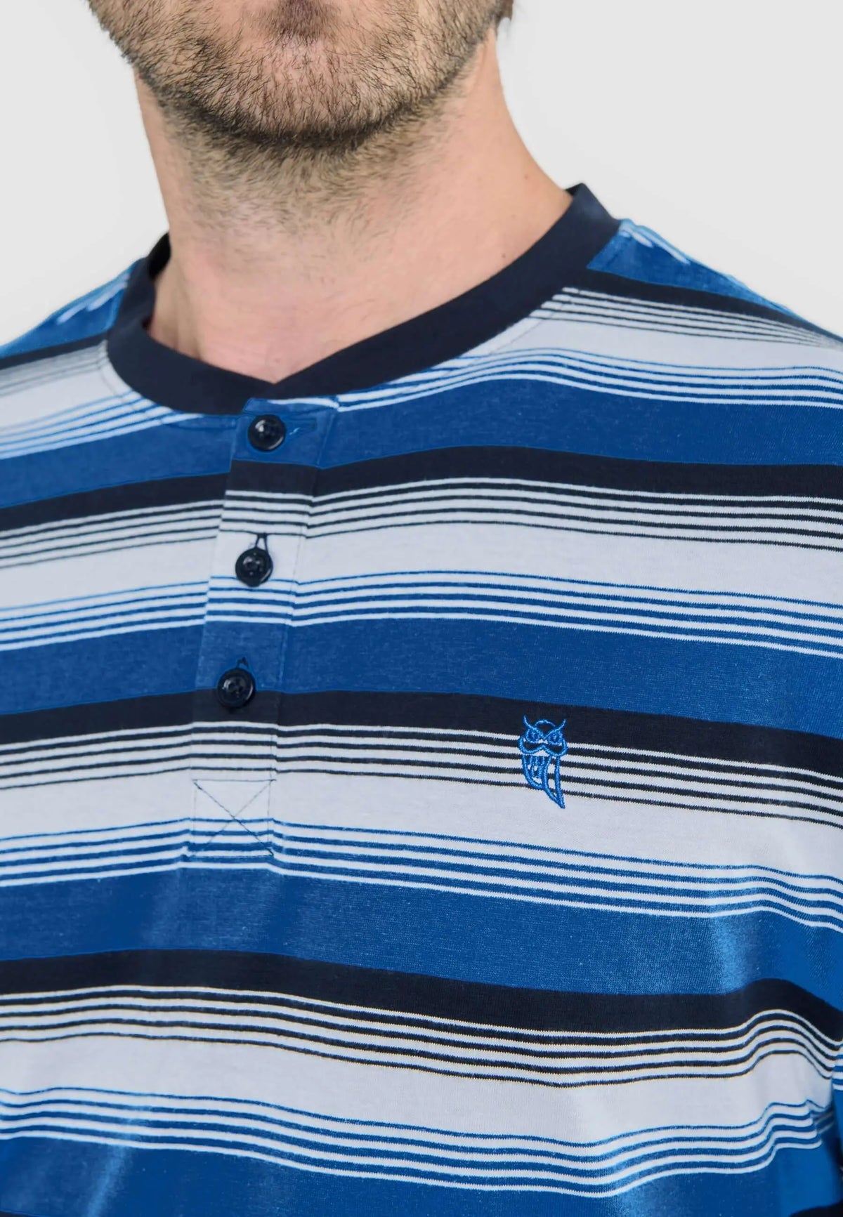 Pijama de hombre a rayas azules y blancas, cuello redondo con tapeta de tres botones y logo de búho bordado en el pecho.
