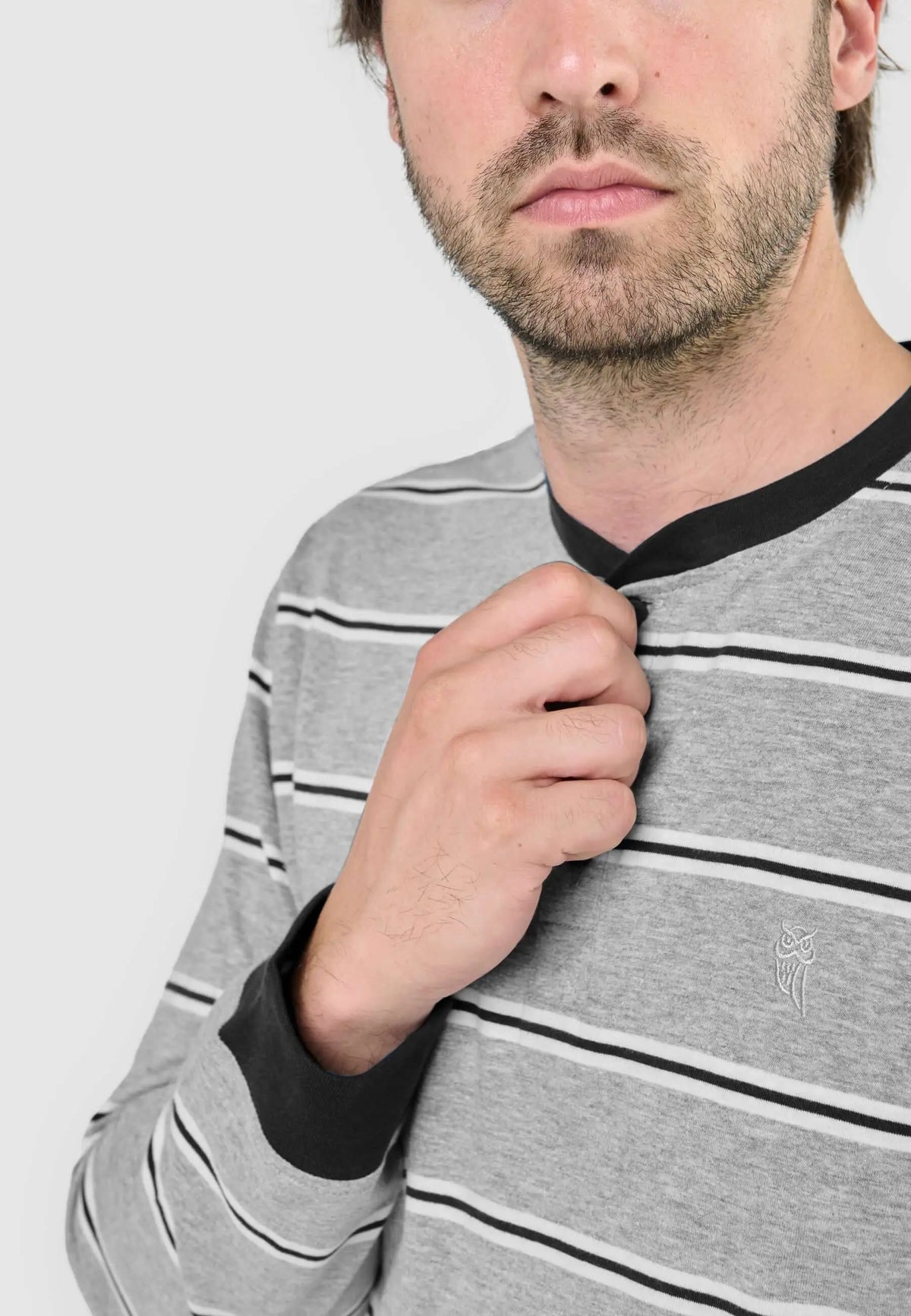 Hombre viste camiseta de pijama gris a rayas negras y blancas, con cuello redondo, tapeta y puños negros.