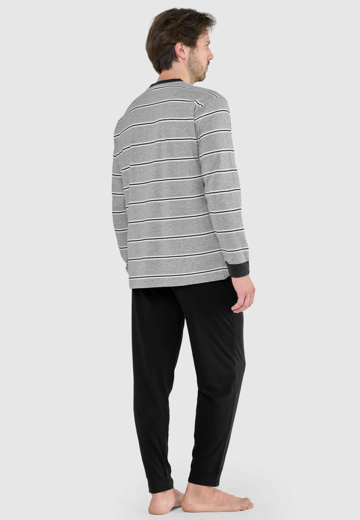 Hombre de espaldas vistiendo pijama de punto: camiseta gris a rayas horizontales con puños negros y pantalón negro liso.