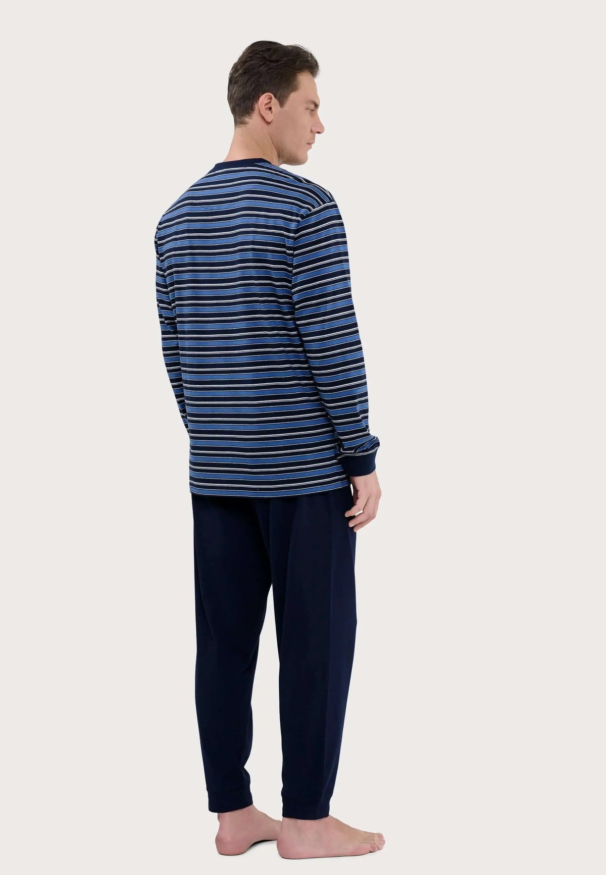 Pijama de hombre con camiseta de rayas azules y pantalón liso azul marino puesto por un modelo de espaldas.