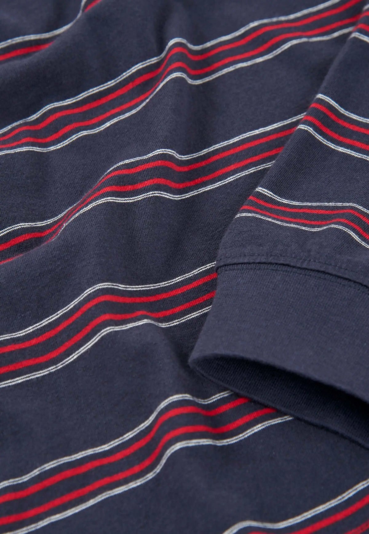 Detalle de tejido de punto de algodón azul marino con rayas horizontales rojas y blancas y puño de manga larga.