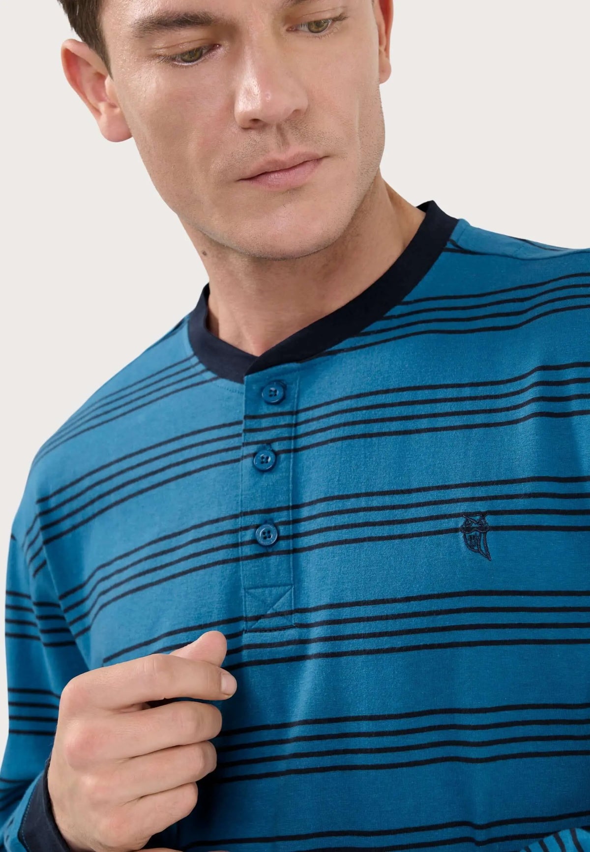 Pijama hombre azul de punto a rayas horizontales negras, cuello redondo, tapeta con tres botones y logo bordado.