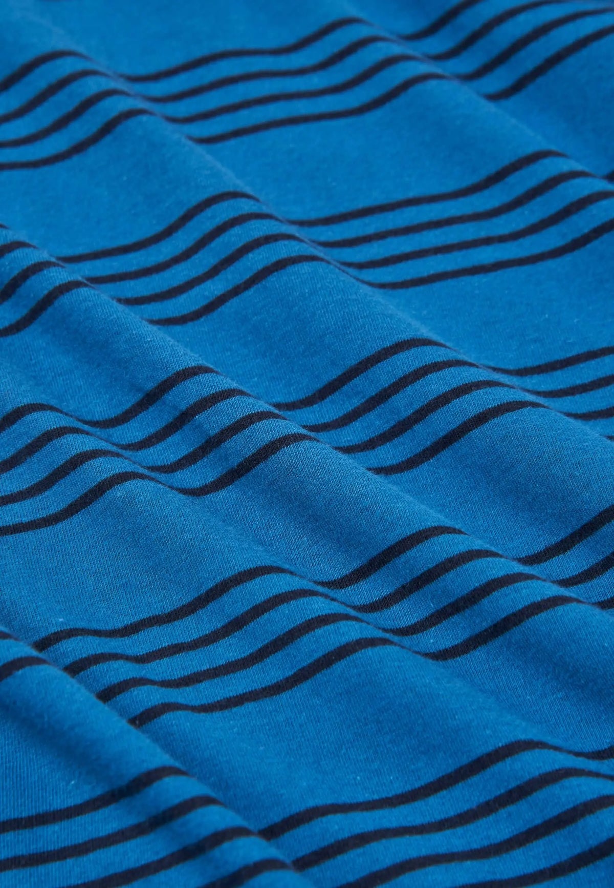 Detalle de tejido de punto azul con estampado de rayas horizontales negras en una prenda doblada con pliegues suaves.
