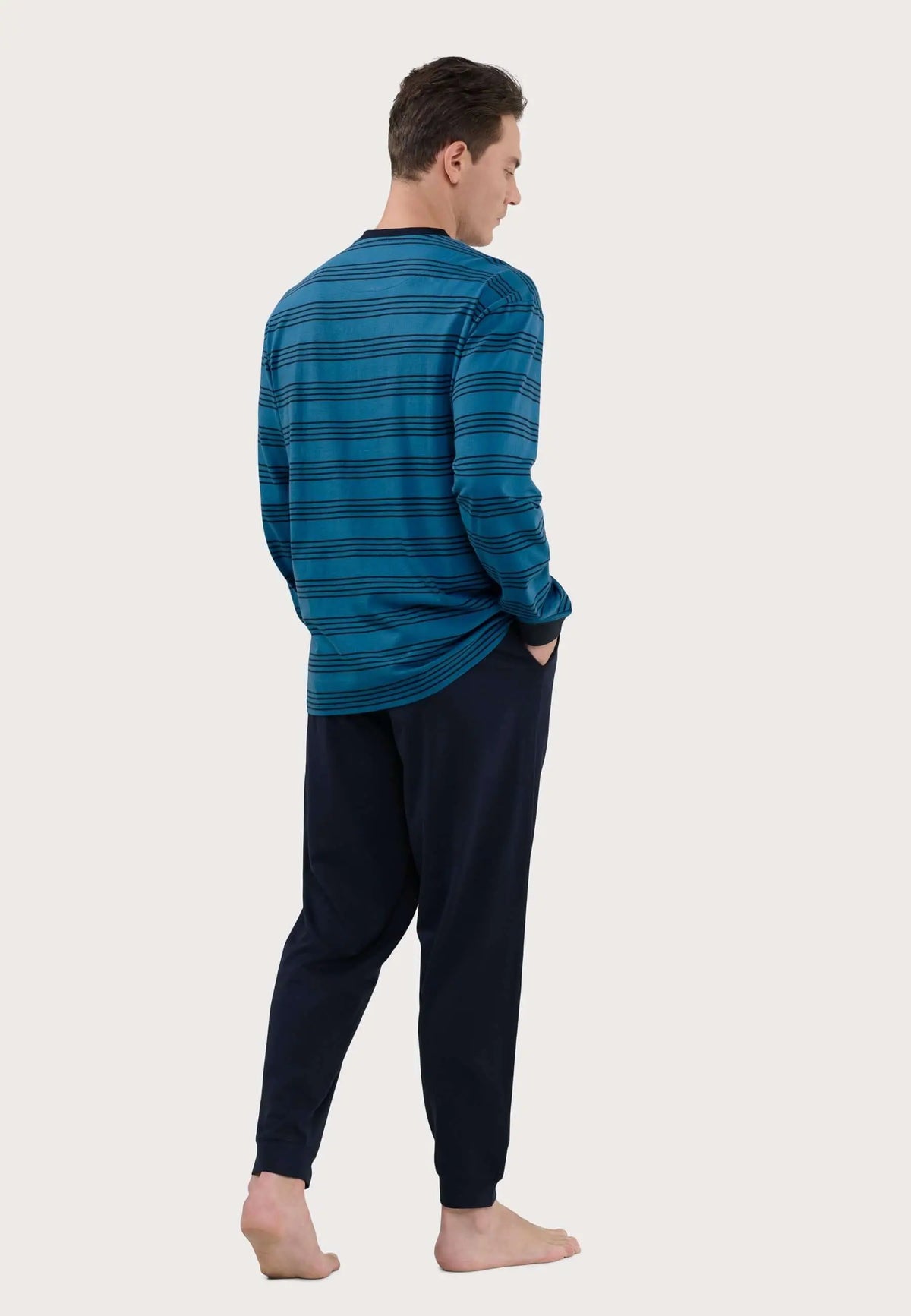 Hombre de espaldas vistiendo pijama de punto: camiseta azul a rayas y pantalón largo liso en azul marino oscuro.
