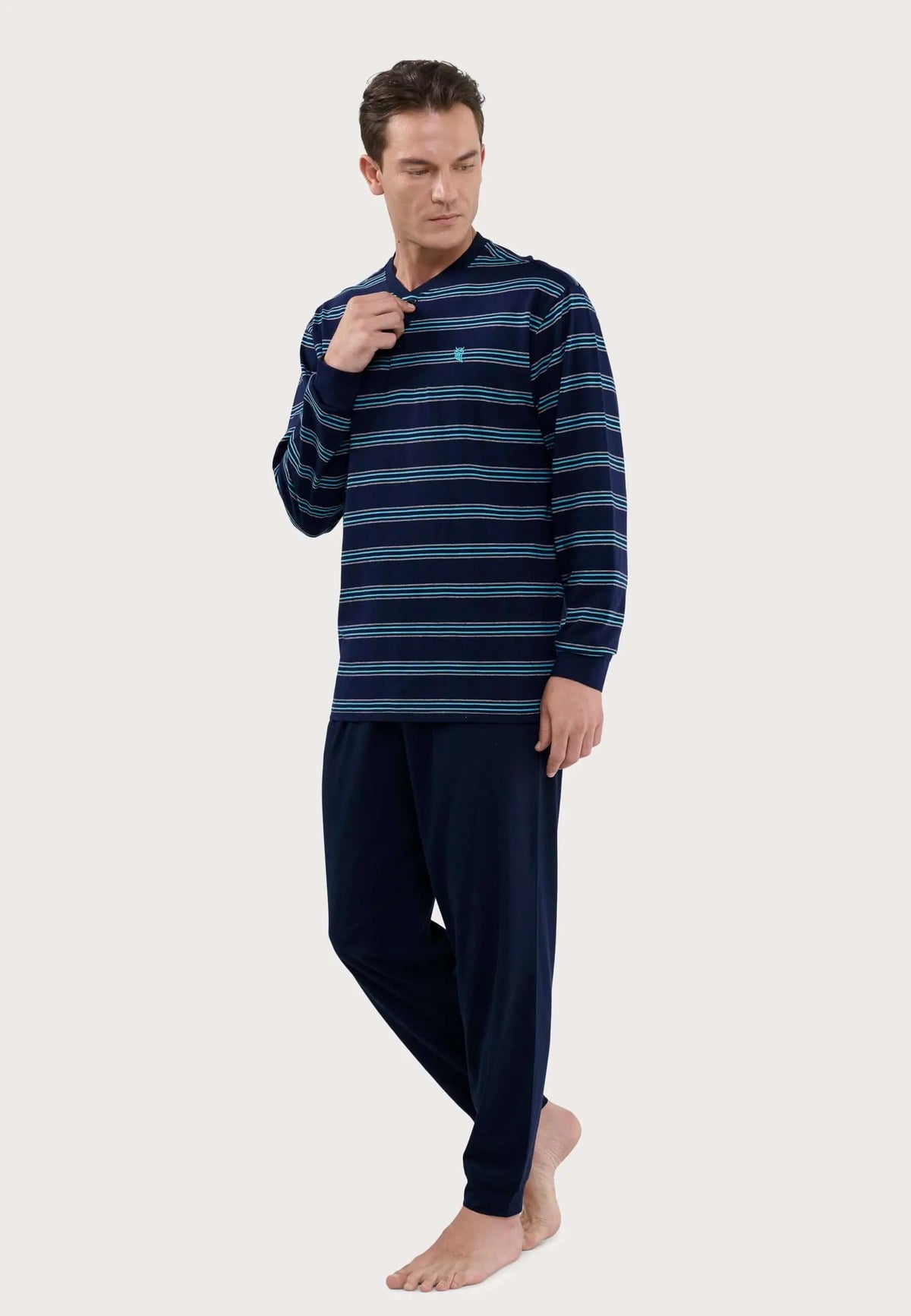 Modelo con pijama de hombre de algodón: camiseta de rayas azules con tapeta y pantalón liso azul marino.