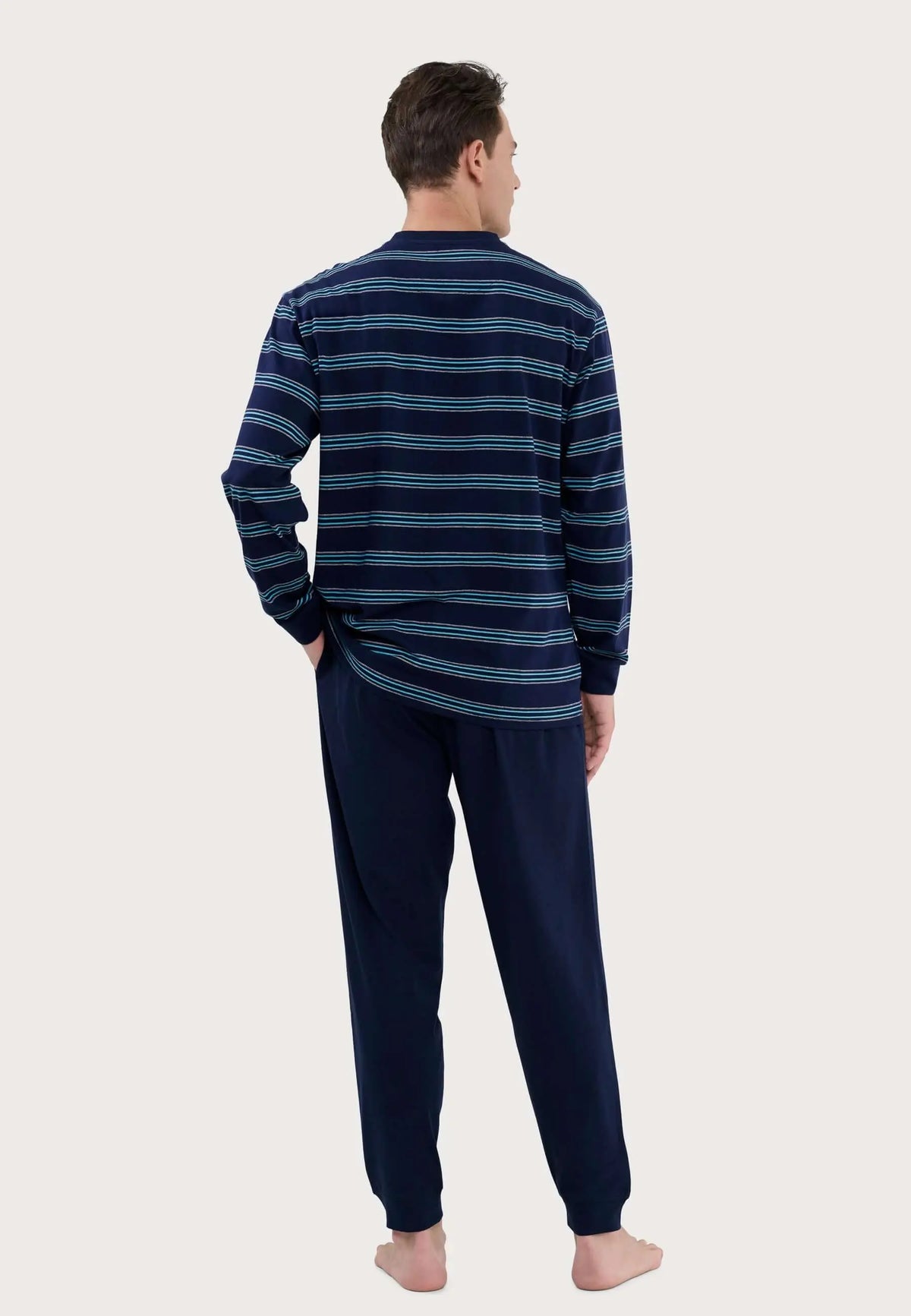 Hombre de espaldas con pijama de punto azul: camiseta de rayas horizontales y pantalón liso, marca El Búho Nocturno.