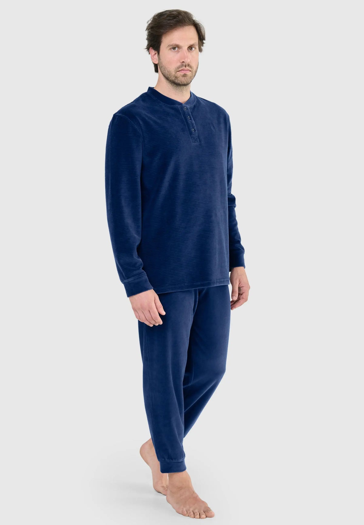 Hombre con pijama azul de terciopelo texturizado, camiseta de botones y pantalón largo, estilo cómodo y cálido.