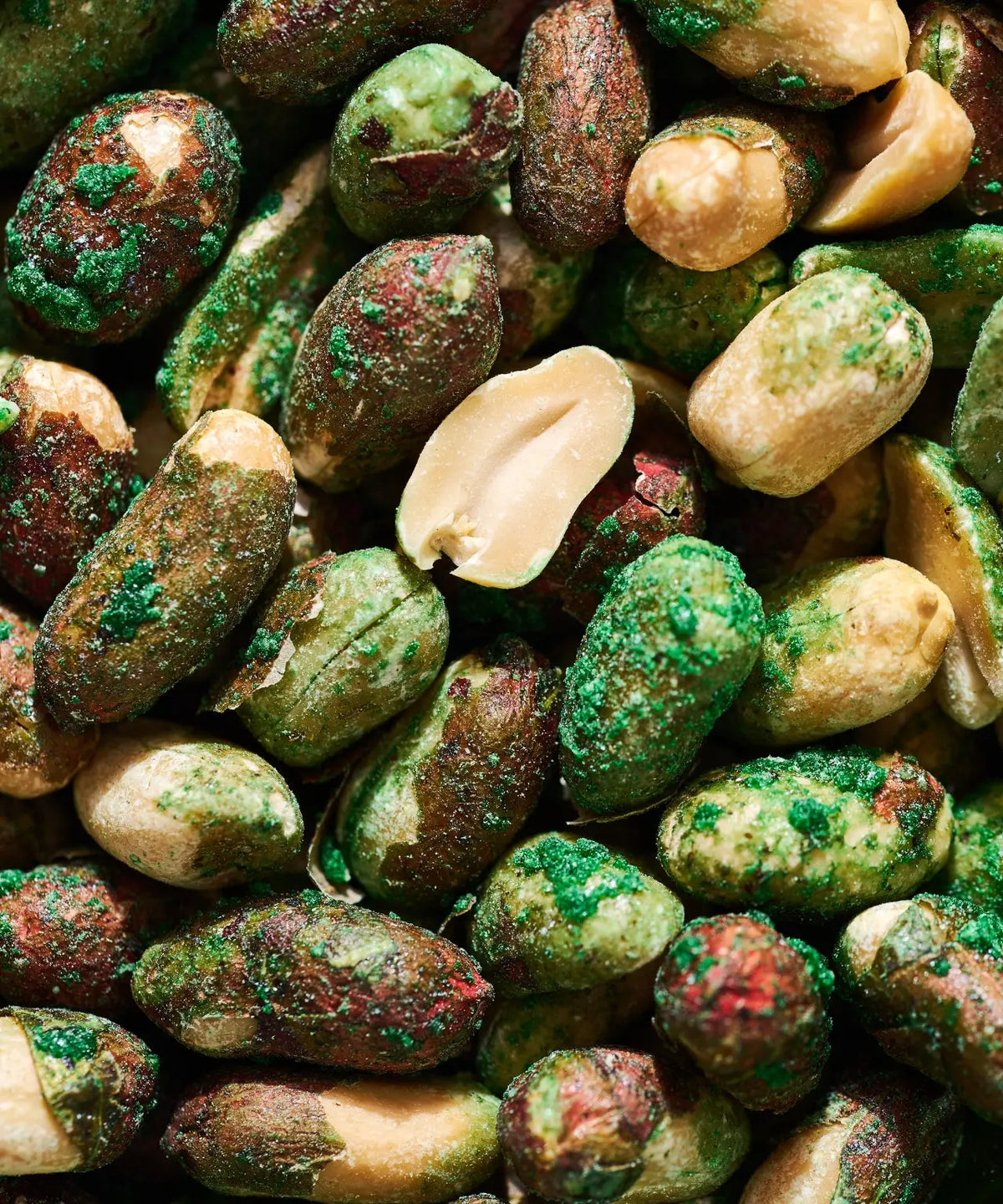 Close-up of roasted peanuts coated in a vibrant green wasabi powder and salt, showing varied textures and shapes.