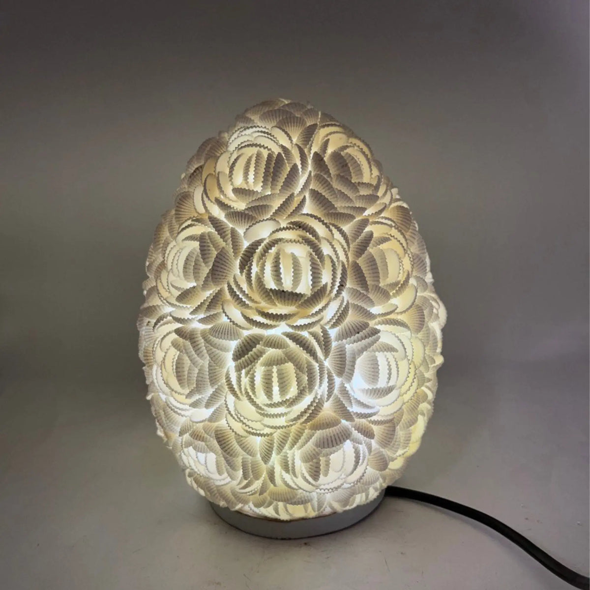 Lámpara boho ovalada de 20cm, hecha con conchas marinas blancas dispuestas en forma de rosas, con luz cálida interna.