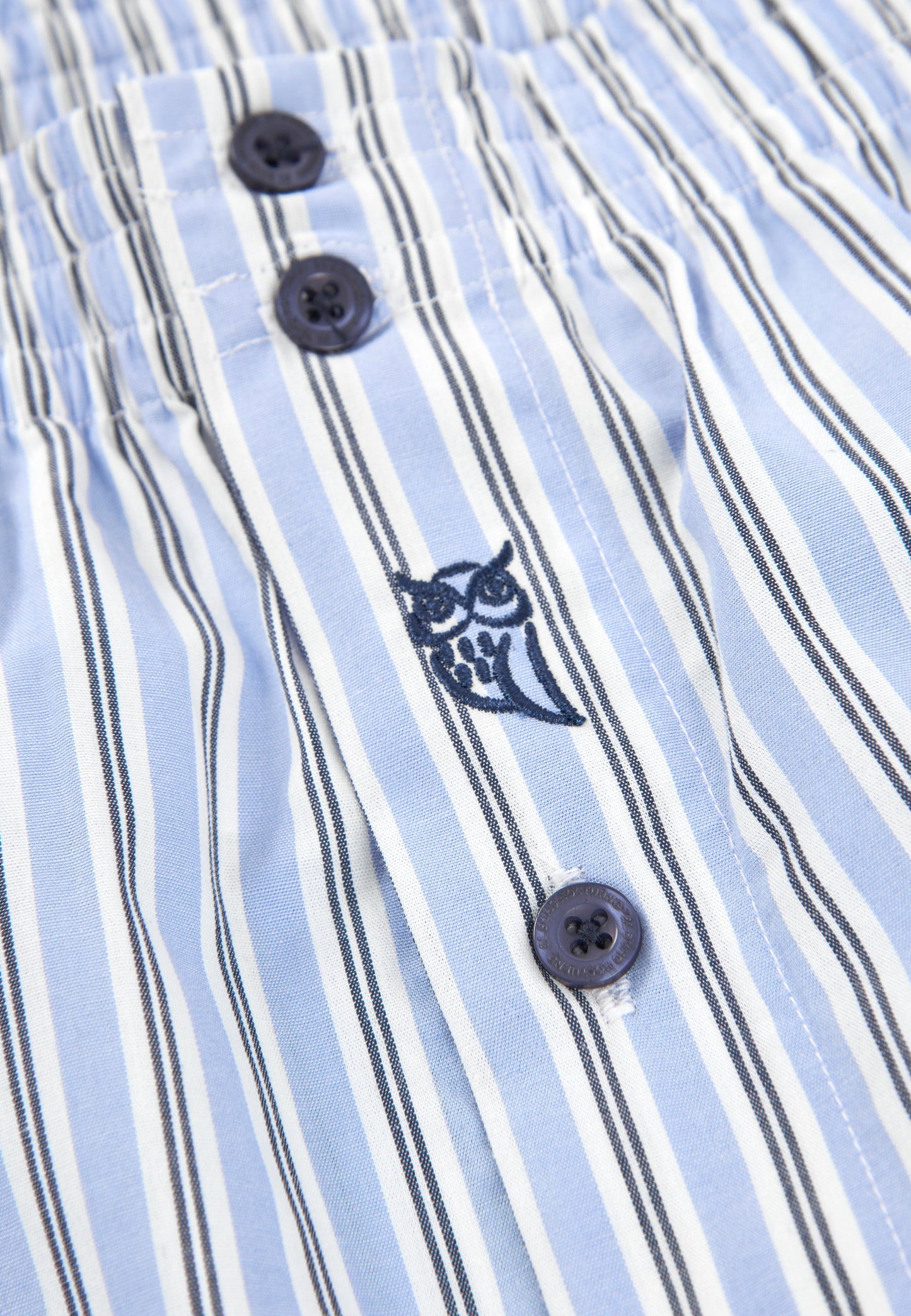 Pantalones cortos de rayas azul claro con botones oscuros y bordado de búho en la parte frontal.