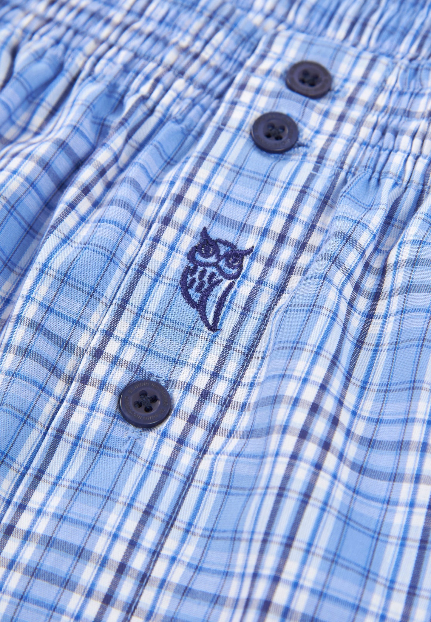 Pantalones cortos de hombre de cuadros en azul con botones y bordado de búho en material ligero.