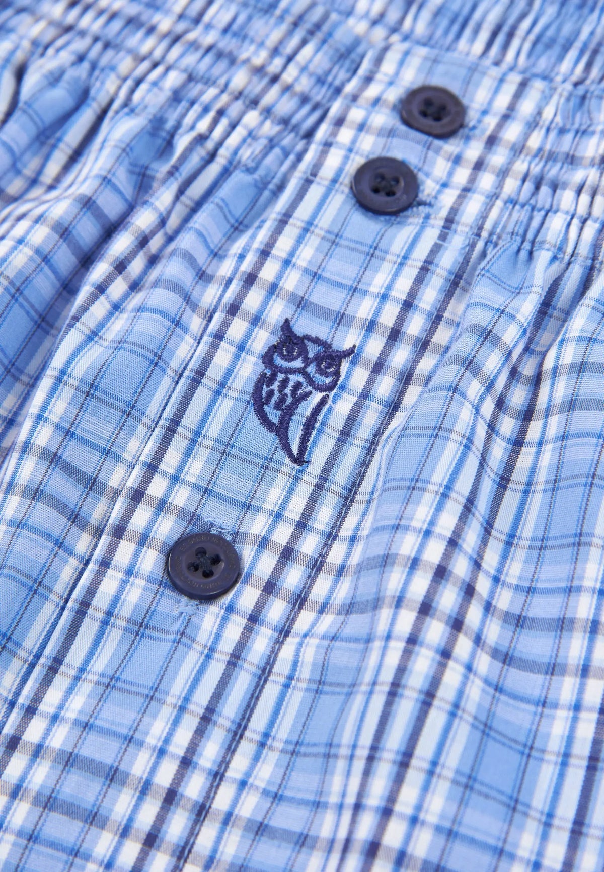 Pantalones cortos de hombre de cuadros en azul con botones y bordado de búho en material ligero.