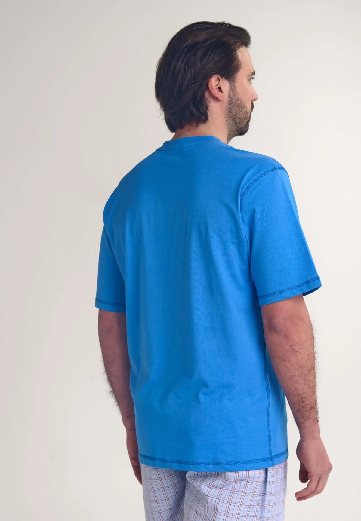 Hombre vistiendo camiseta de pijama azul de algodón, manga corta, corte recto y estilo casual sobre fondo claro.