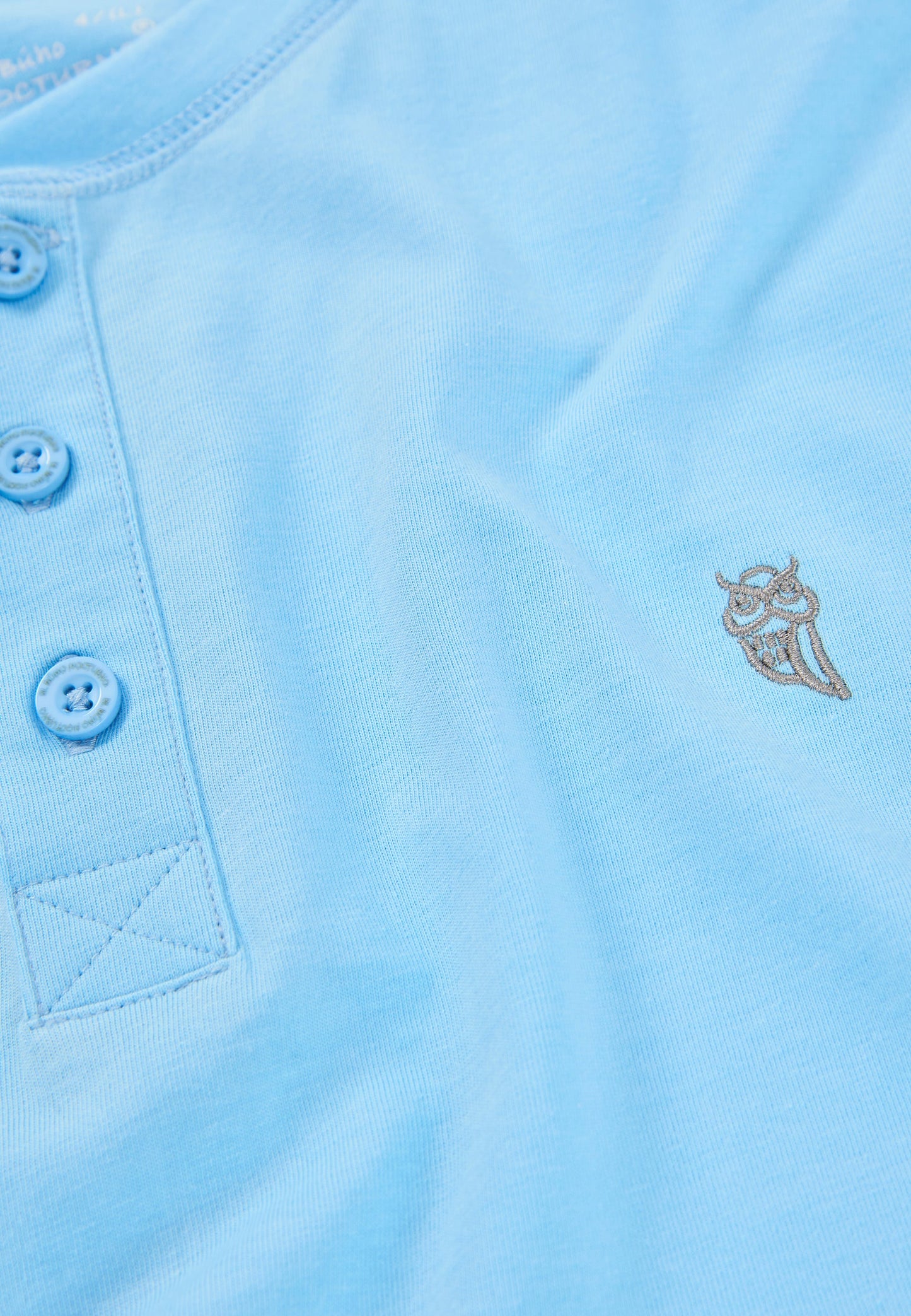 Camiseta de algodón azul claro con botones y diseño de buho bordado. Ideal para un look casual y cómodo.
