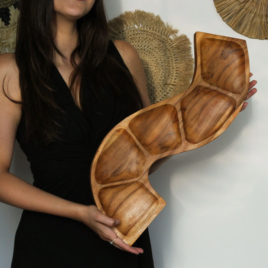 Cuenco de madera de teca con forma de serpiente y cinco compartimentos, sostenido por una mujer. Textura natural.