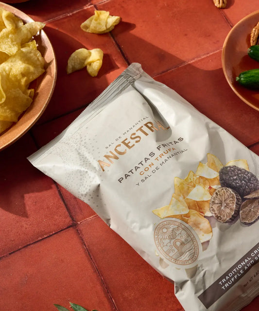 Bag of truffle potato chips with spring salt, on a terracotta surface with bowls of snacks.