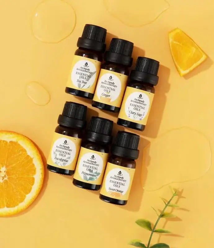 Six amber glass essential oil bottles with black caps on a yellow background, decorated with orange slices and oil.