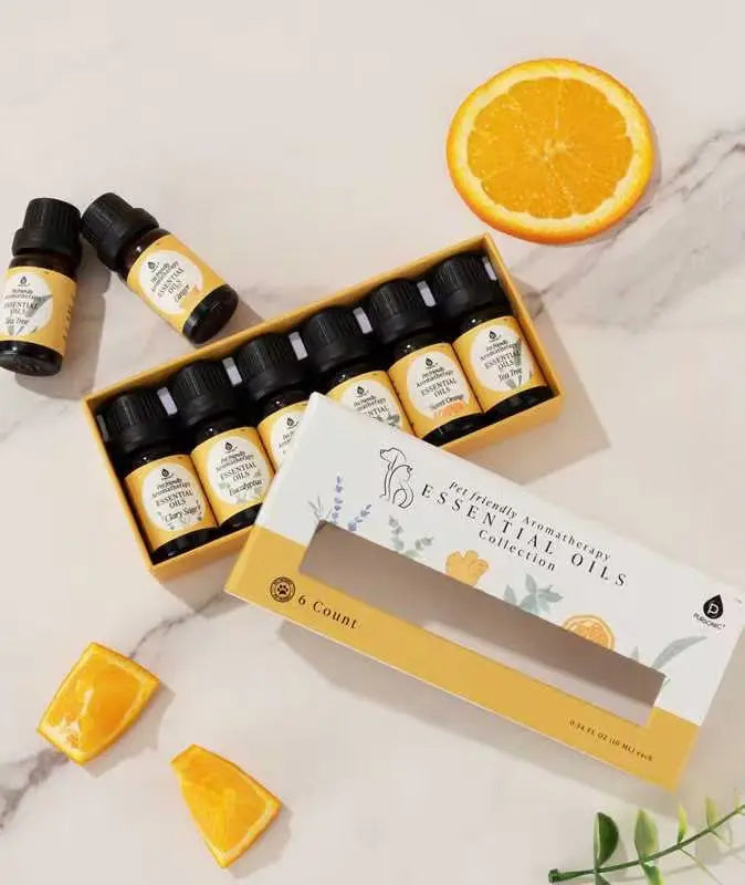 Pet-friendly essential oils collection in a yellow box, with amber glass bottles, citrus slices on a marble surface.
