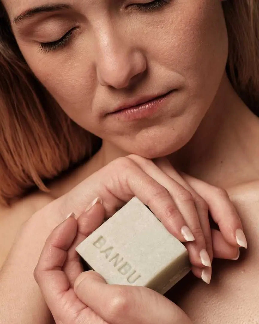 Mujer con ojos cerrados sostiene una pastilla de mousse facial sólida Banbu de color verde claro y textura natural.