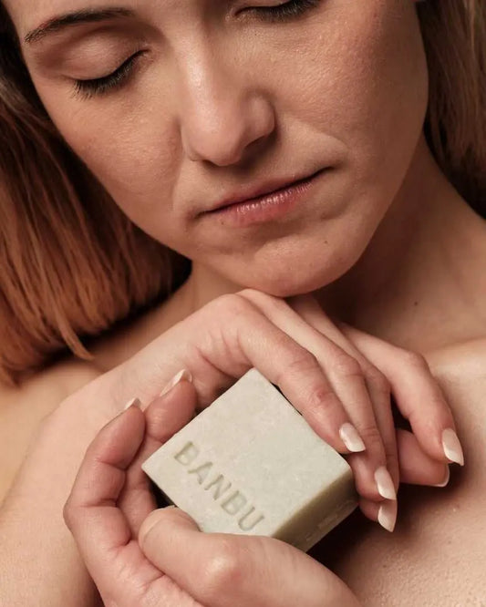 Mujer con ojos cerrados sostiene una pastilla de mousse facial sólida Banbu de color verde claro y textura natural.