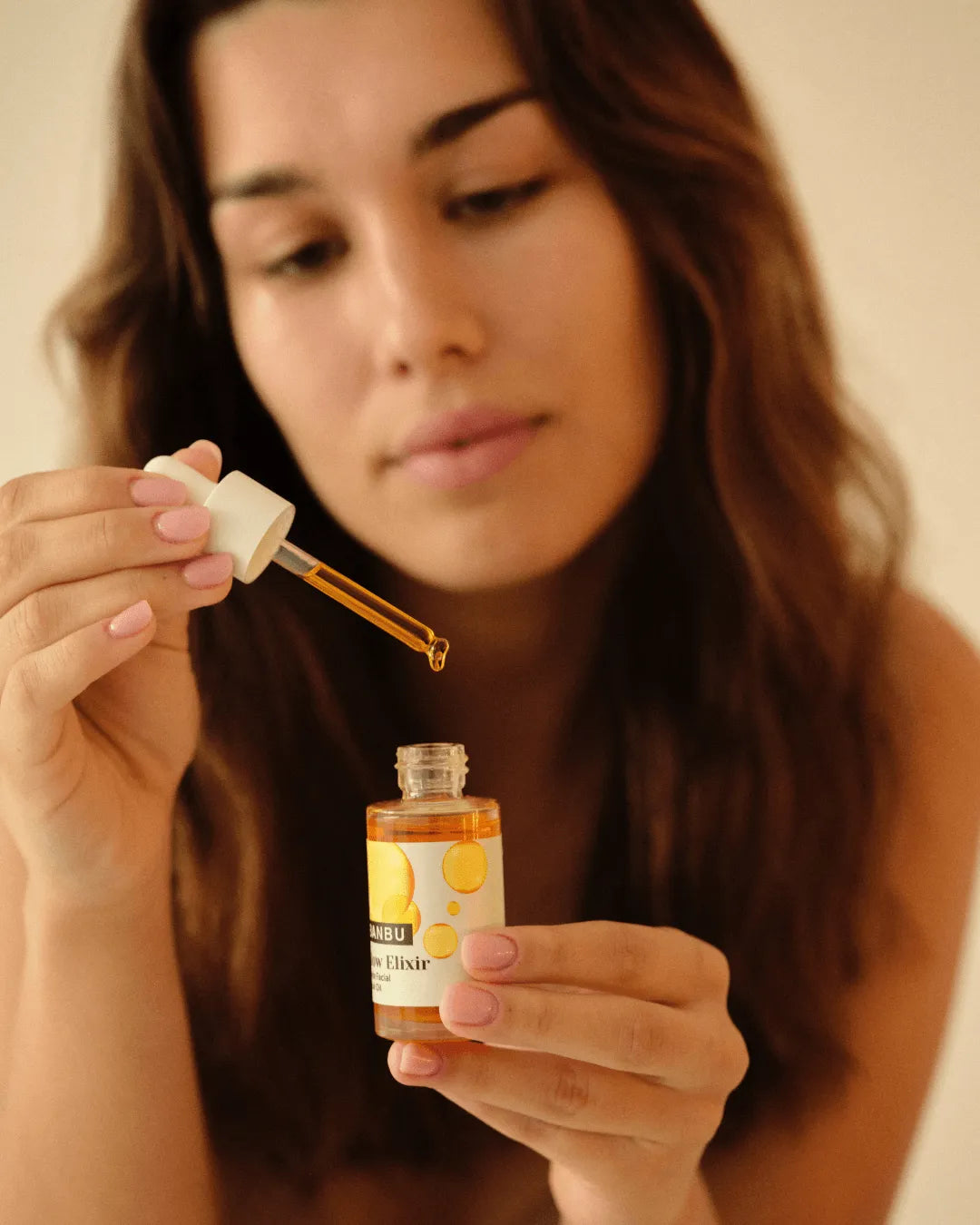 Mujer usando el sérum Glow Elixir de Banbu: un aceite facial dorado en frasco de vidrio con gotero.