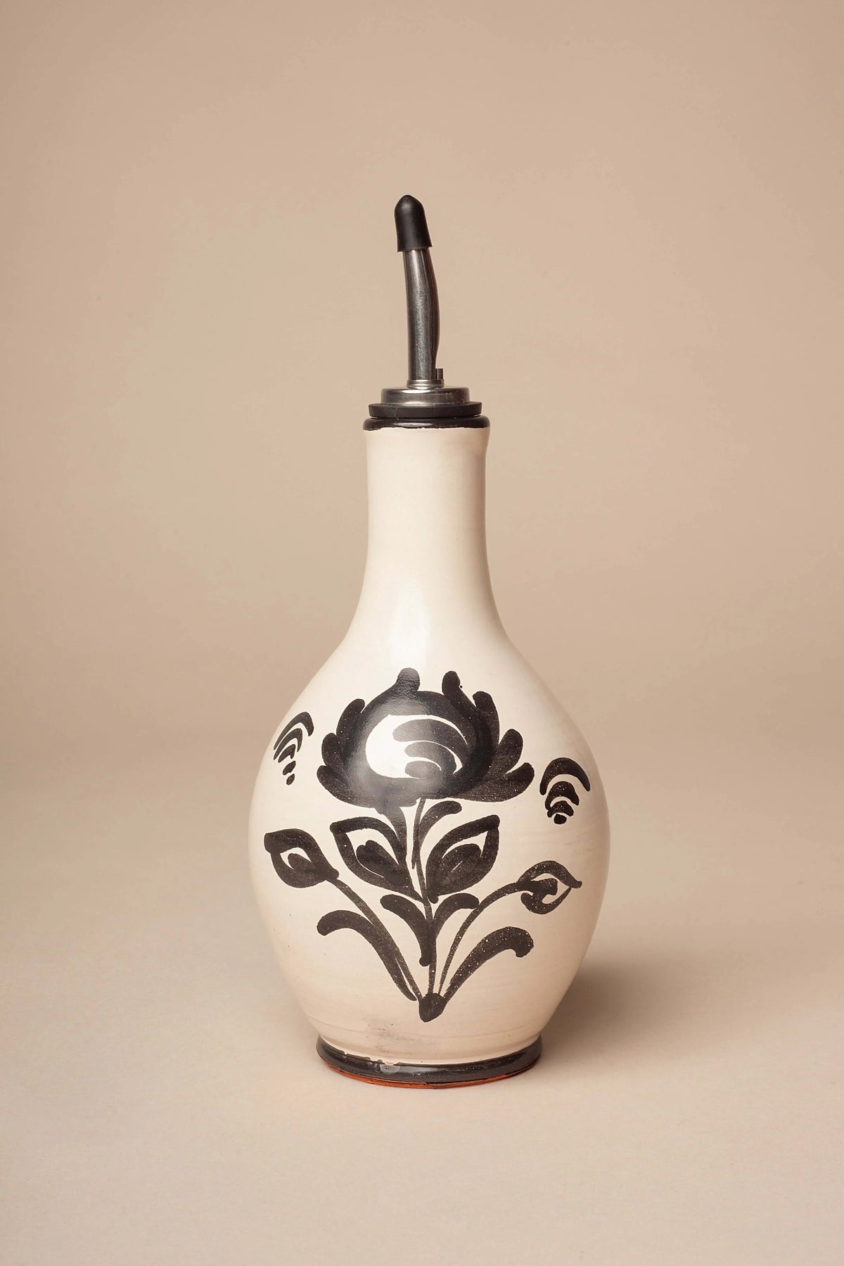 Aceitera de cerámica crema con forma de pera y dibujo floral en negro, rematada con un vertedor de metal.