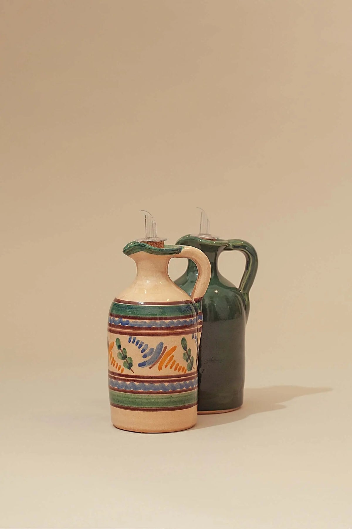 Dos aceiteras de cerámica artesanal, una decorada con motivos vegetales y otra verde brillante, con tapón vertedor.