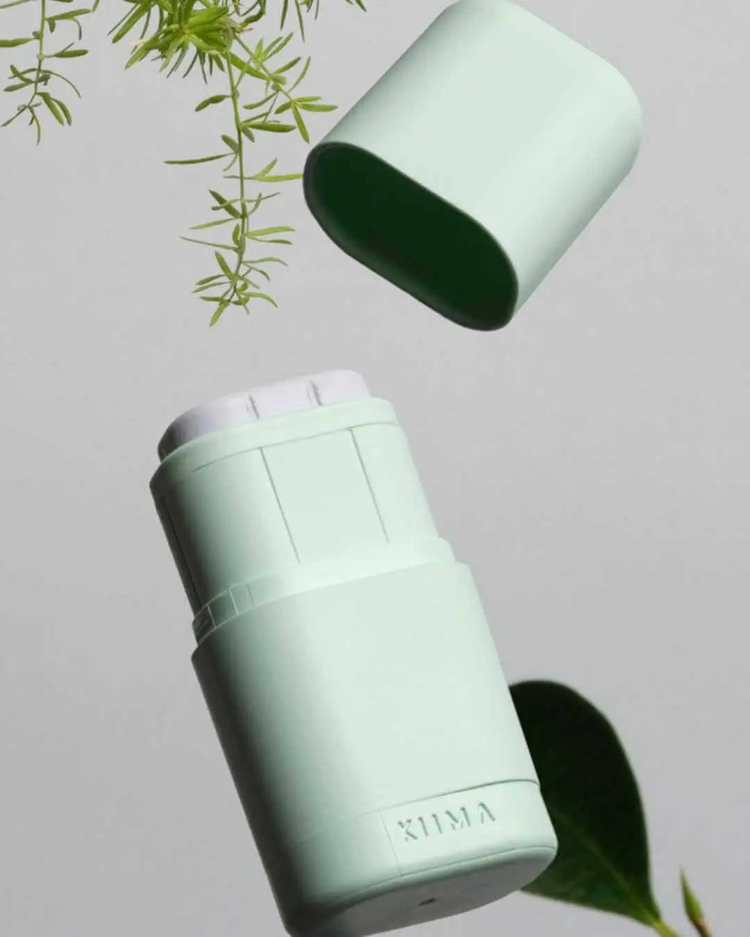 Desodorante sólido Banbu con aplicador verde menta y tapa abierta sobre fondo gris con vegetación. Diseño ecológico.