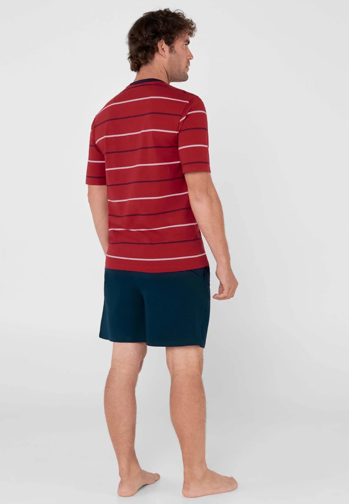 Hombre de espaldas con pijama corto: camiseta roja de rayas horizontales y pantalón corto liso de color azul marino.